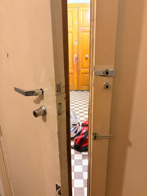 Porte d'appartement ouverte sur le palier d'un immeuble ancien, serrure et verrou intacts
